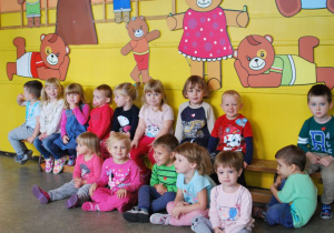 Grupa uśmiechniętych dzieci siedzi na ławce i na podłodze w szatni przedszkolnej