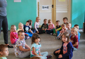 Grupa uśmiechniętych dzieci siedzi na podłodze w szatni przedszkolnej