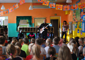 Mężczyzna gra na gitarze elektrycznej w szatni przedszkolnej przed grupą dzieci