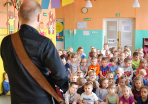 Mężczyzna gra na gitarze elektrycznej w szatni przedszkolnej przed grupą dzieci