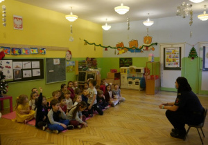 Dzieci w przedszkolu siedzą w kręgu i słuchają strażnika miejskiego