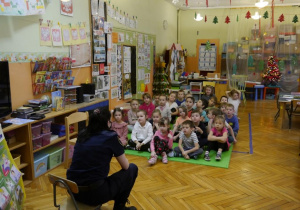 Dzieci w przedszkolu siedzą w kręgu i słuchają strażnika miejskiego
