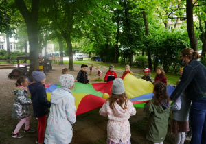 grupa dzieci bawiąca się chustą animacyjną w ogrodzie przedszkolnym
